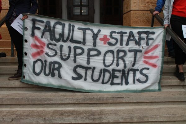 Faculty protest outside of Bascom Hall. Two faculty hold this sign reading "FACULTY + STAFF SUPPORT OUR STUDENTS." May 2, 2024.